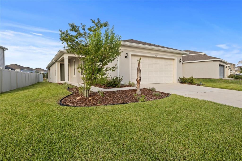 A single-story house with a beige exterior, a two-car garage, and a landscaped front yard — 7311 CATANIA LOOP, CLERMONT, FL