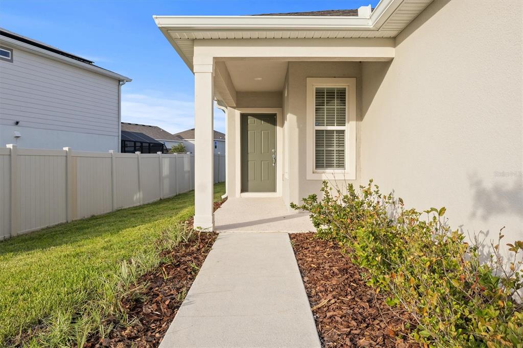 A concrete walkway leads to the covered front porch of a house with beige siding — 7311 CATANIA LOOP, CLERMONT, FL