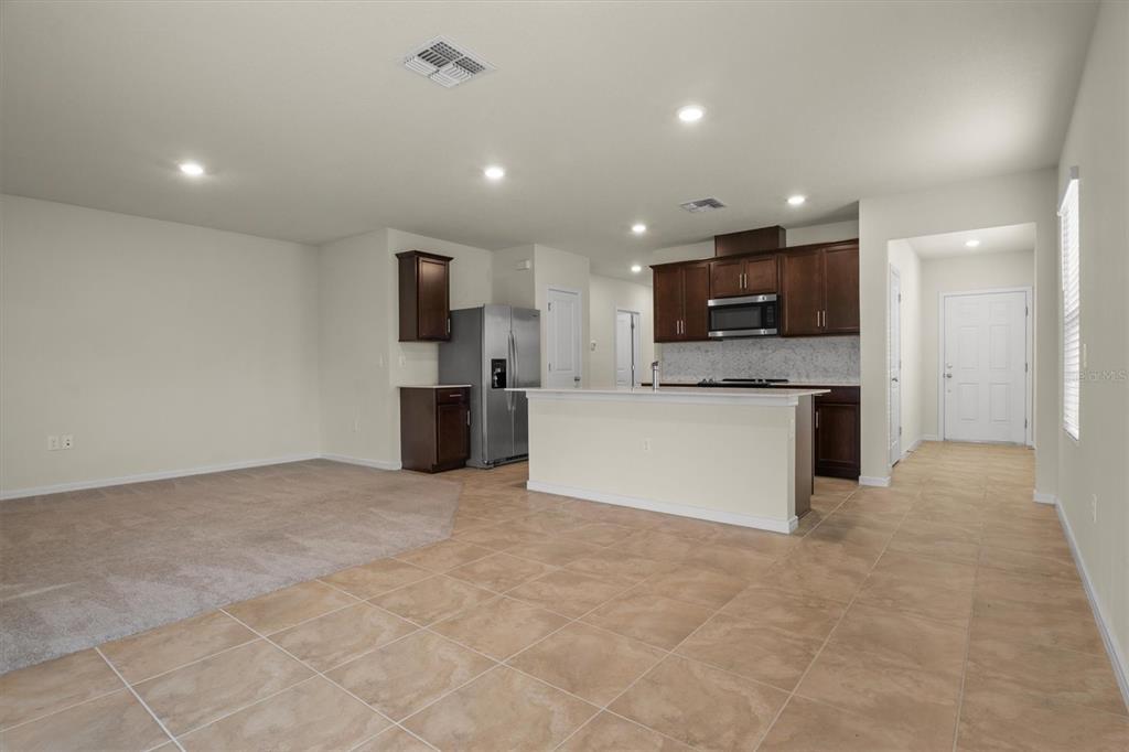 An open-concept kitchen with dark cabinets and a central island overlooks a carpeted living area — 7311 CATANIA LOOP, CLERMONT, FL