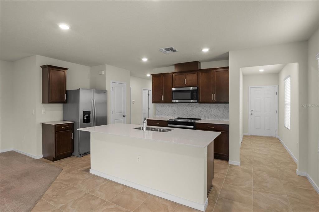 A kitchen features dark wood cabinets, stainless steel appliances, a white island, and tile flooring — 7311 CATANIA LOOP, CLERMONT, FL