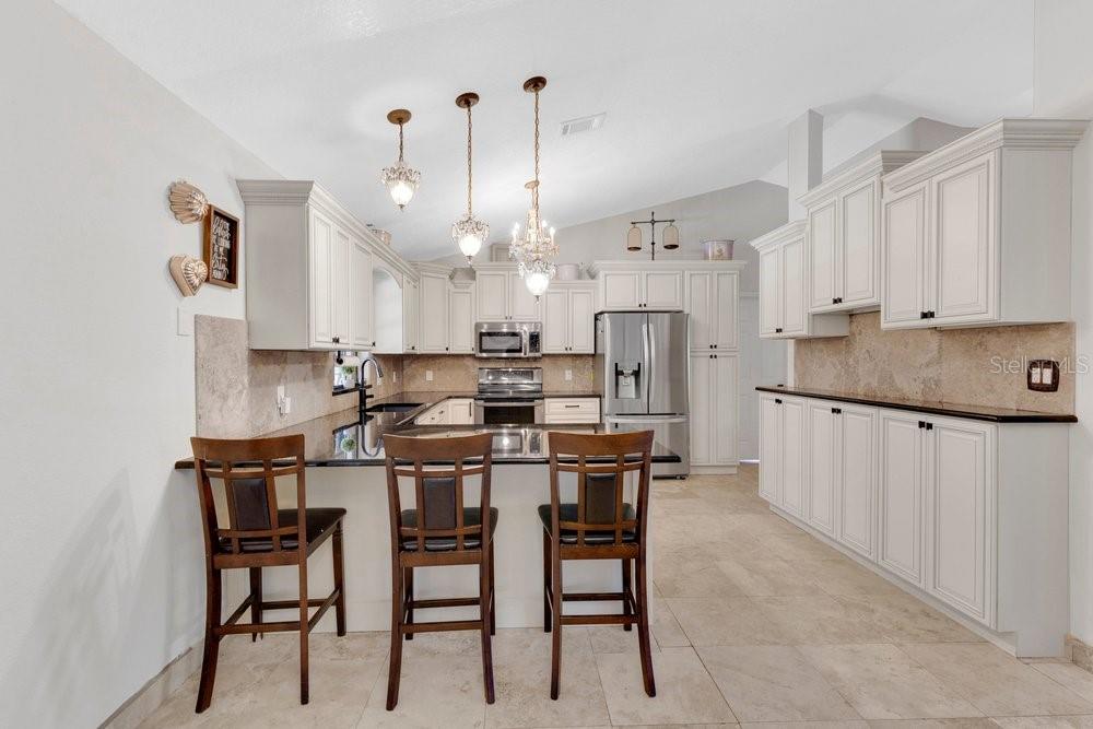 A kitchen with white cabinets, dark granite countertops, stainless steel appliances, and three bar stools — 1304 ARIANA WOODS CIRCLE, AUBURNDALE, FL