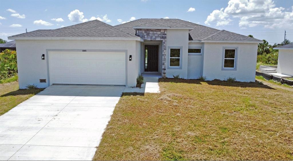 A single-story house with a white stucco exterior, stone accents, and a two-car garage — 13558 JERONIMO LANE, PORT CHARLOTTE, FL