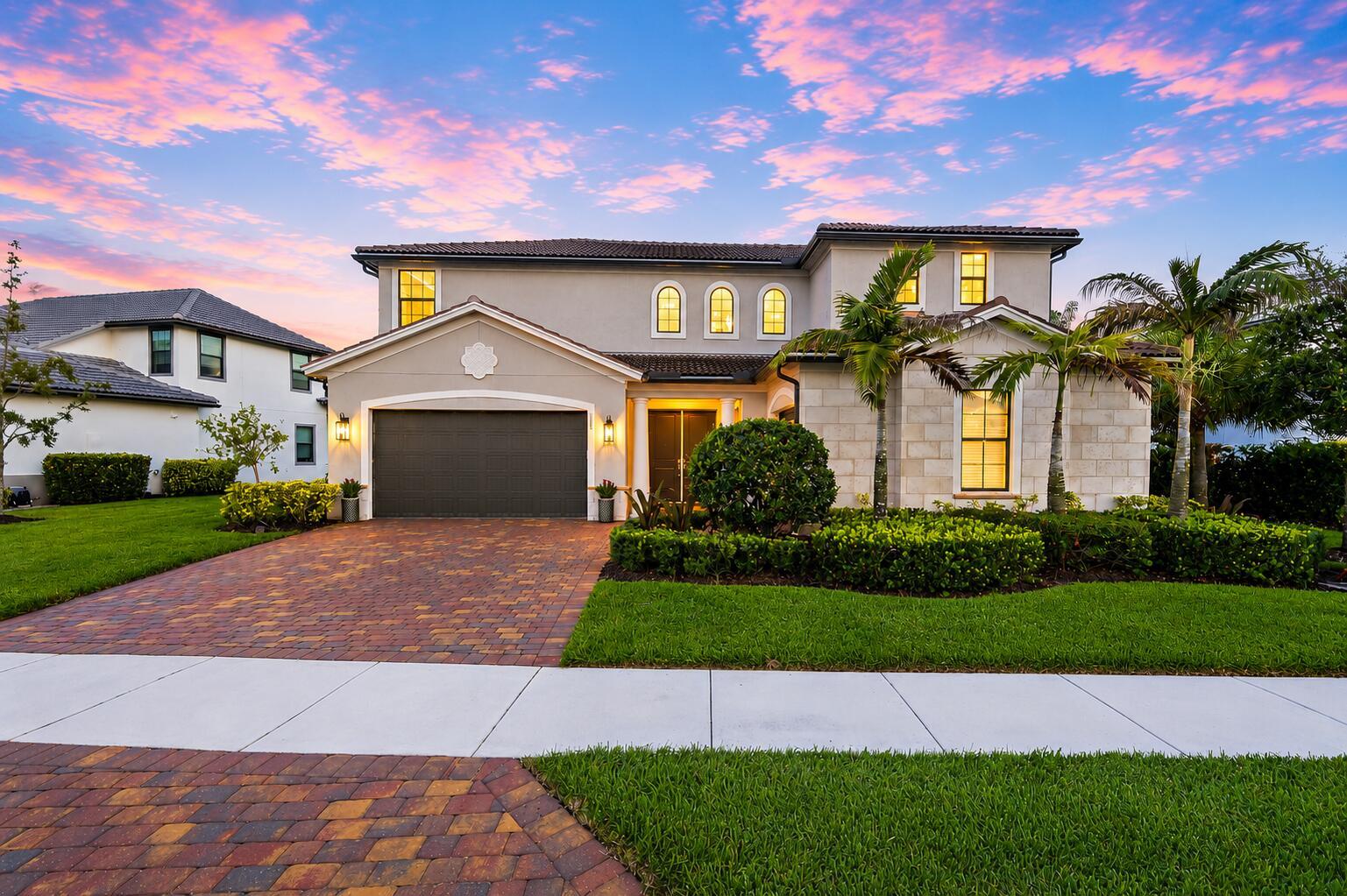 A two-story suburban house with a paved driveway, a garage, and palm trees at dusk — 315 Sonoma Isles Circle, Jupiter FL 33478, JUPITER, FL