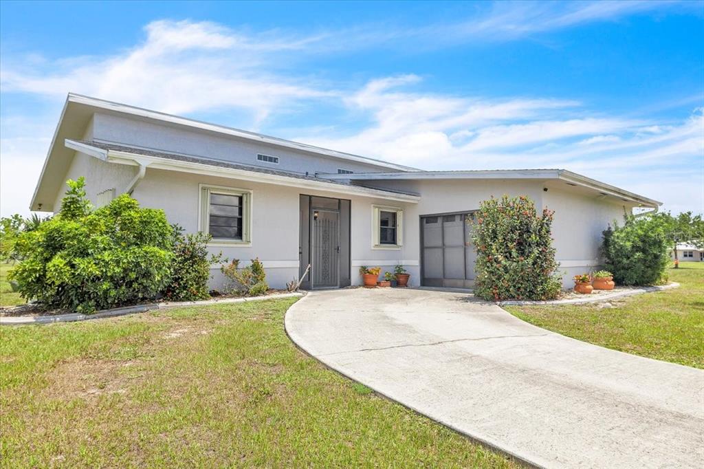 A single-story house with a light-colored exterior, a concrete driveway, and a screened front entryway — 25313 DELGADO DRIVE, PUNTA GORDA, FL