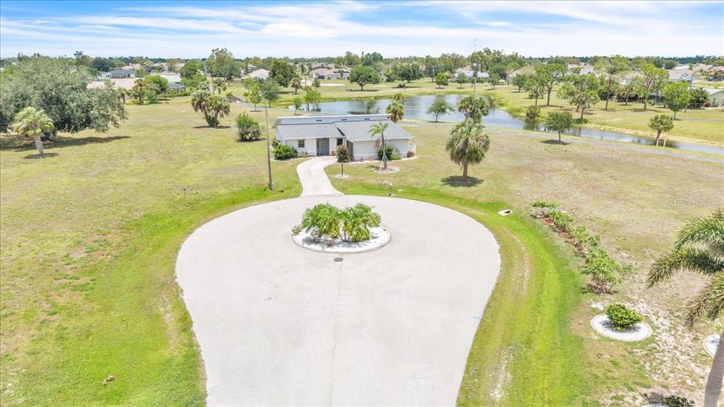 An aerial view shows a single-story house with a circular driveway and a pond — 25313 DELGADO DRIVE, PUNTA GORDA, FL