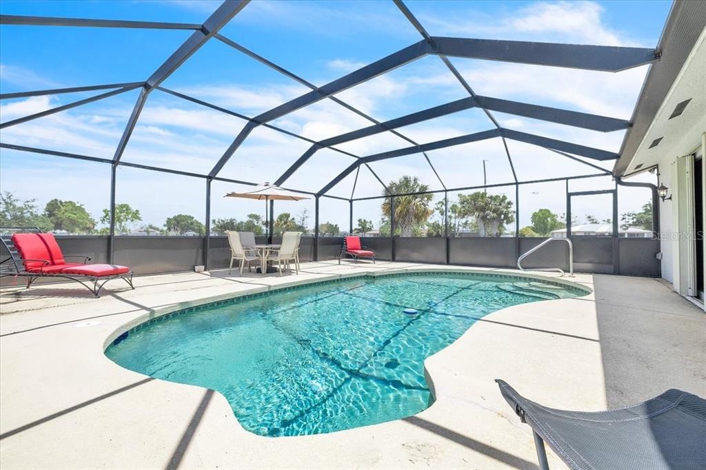 A swimming pool sits inside a screened-in lanai with patio furniture and a concrete deck — 25313 DELGADO DRIVE, PUNTA GORDA, FL