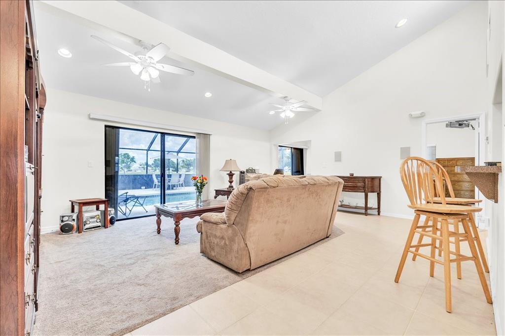 A living room with beige carpet, a tan sofa, ceiling fans, and sliding glass doors — 25313 DELGADO DRIVE, PUNTA GORDA, FL