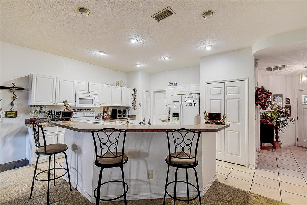 A kitchen features white cabinets, a breakfast bar with three stools, and tile flooring — 14985 ALAN COURT, LARGO, FL