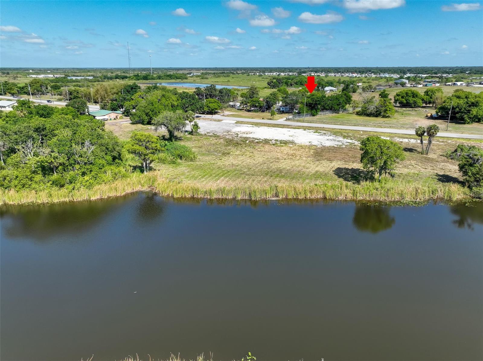 An aerial view shows a pond in the foreground and a vacant lot with trees — 615 State Road 78, Okeechobee FL 34974, OKEECHOBEE, FL