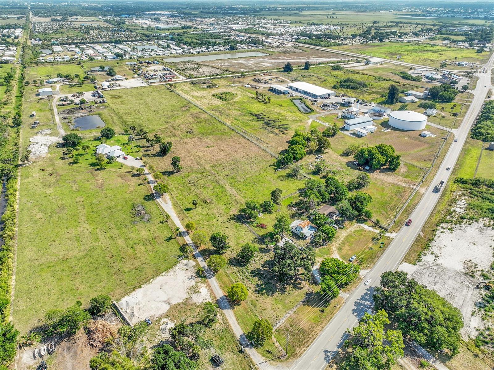 An aerial view shows a large grassy lot with two houses, trees, and nearby industrial facilities — 615 State Road 78, Okeechobee FL 34974, OKEECHOBEE, FL