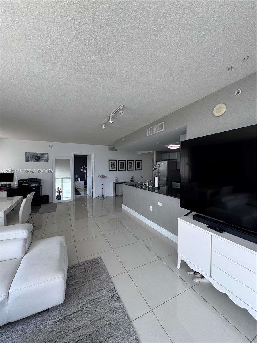 An open-concept living area features white tile flooring, a kitchen island, and a large television — 1861 NW S River Dr # 906, Miami FL 33125, MIAMI, FL