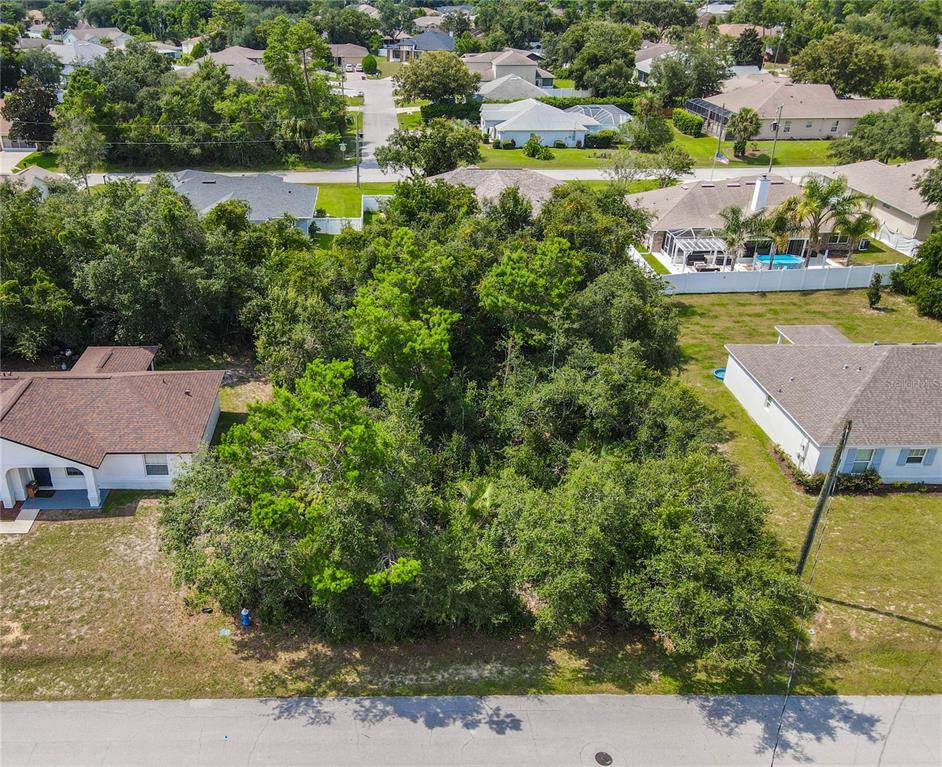 An aerial view shows a vacant, tree-covered residential lot situated between two existing houses — 76 FREEPORT LANE, PALM COAST, FL