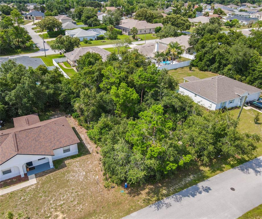 An aerial view shows a vacant, tree-covered lot situated between two single-family homes — 76 FREEPORT LANE, PALM COAST, FL