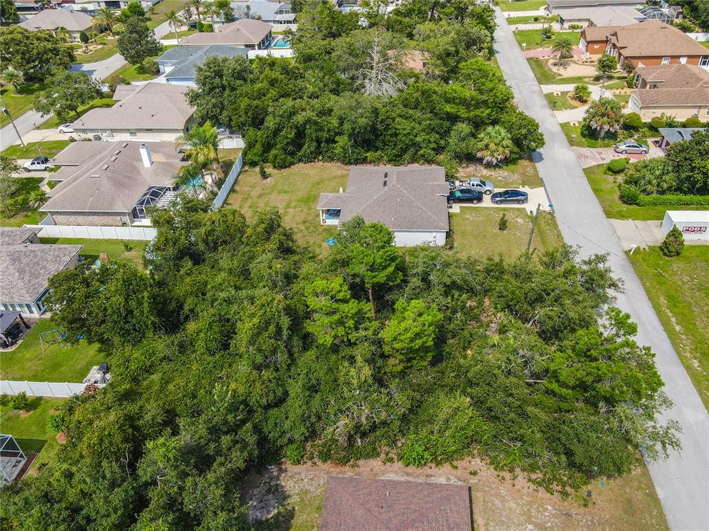 An aerial view shows a residential house surrounded by dense trees and a paved street — 76 FREEPORT LANE, PALM COAST, FL