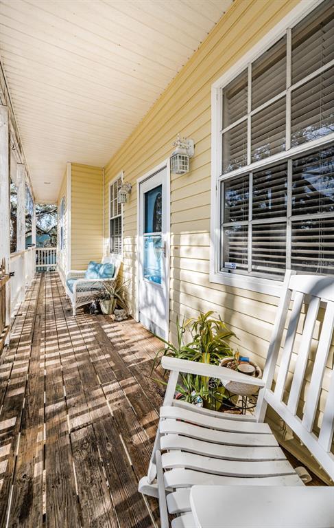 A covered wooden porch features a white wicker sofa with blue cushions and a rocking chair — 5127 BAY BOULEVARD, PORT RICHEY, FL
