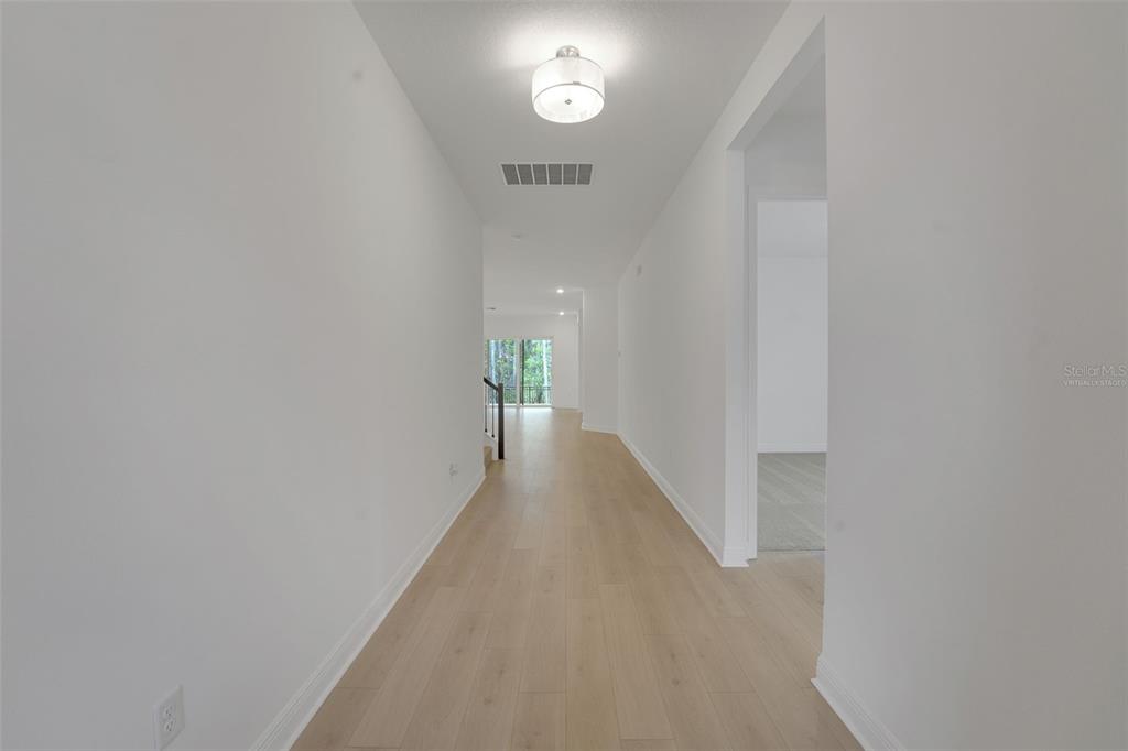 A long, white-walled hallway features light wood-look flooring and a modern ceiling light fixture — 14353 CREST PALM AVENUE, WINDERMERE, FL