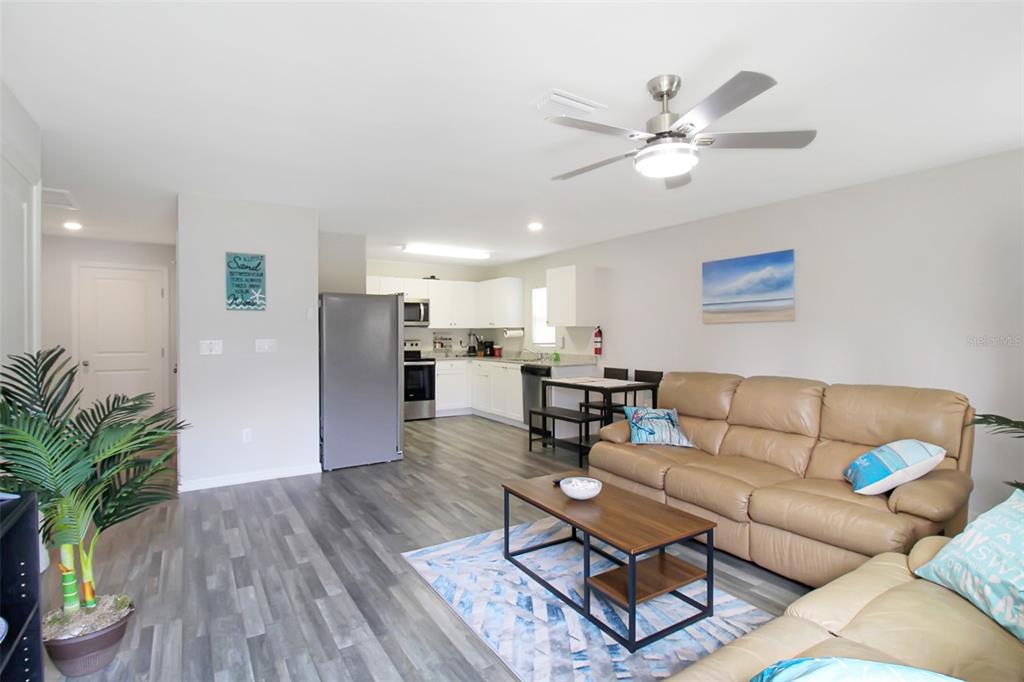 An open-concept living room and kitchen featuring light wood-look flooring and tan leather sofas — 3084 SUDBURY STREET, PORT CHARLOTTE, FL
