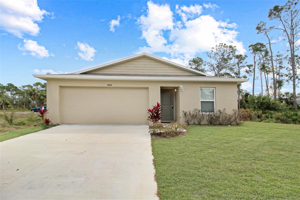 A single-story house with a beige stucco exterior, a two-car garage, and a front lawn — 3084 SUDBURY STREET, PORT CHARLOTTE, FL