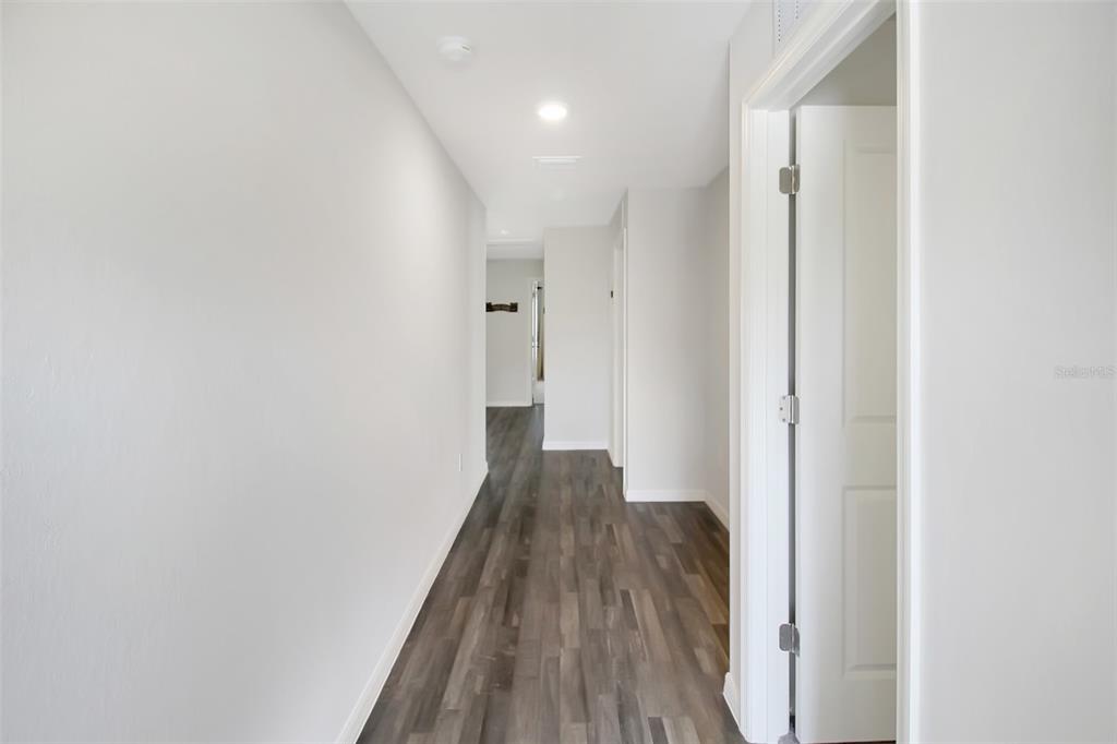 A hallway with light gray walls and dark wood-look flooring leads toward a distant doorway — 3084 SUDBURY STREET, PORT CHARLOTTE, FL