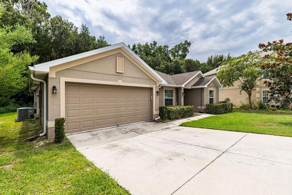 A single-story house with a beige stucco exterior, a two-car garage, and a concrete driveway — 7830 SLOEWOOD DRIVE, LEESBURG, FL