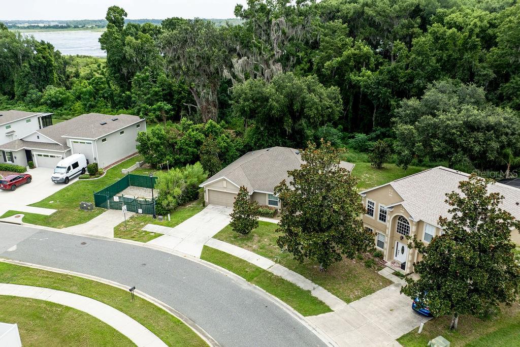 An aerial view shows three suburban houses with driveways and lawns near a wooded area — 7830 SLOEWOOD DRIVE, LEESBURG, FL