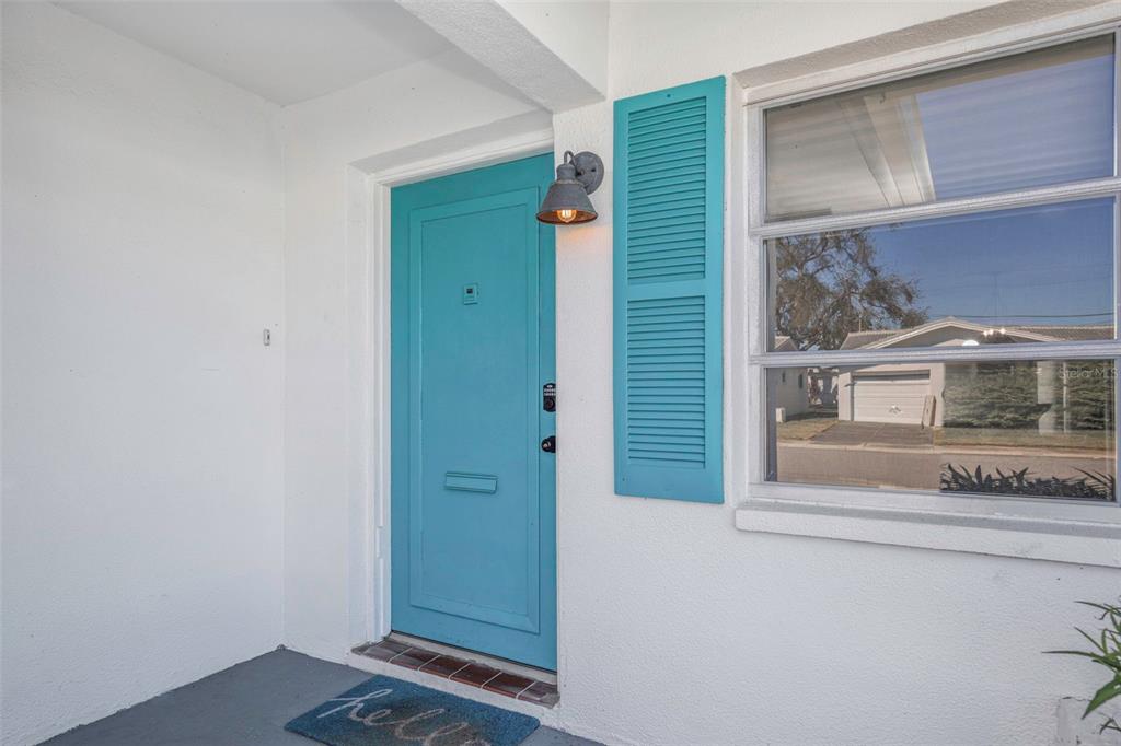 A bright blue front door with matching shutters sits on a white exterior porch — 4488 100TH AVENUE N, PINELLAS PARK, FL
