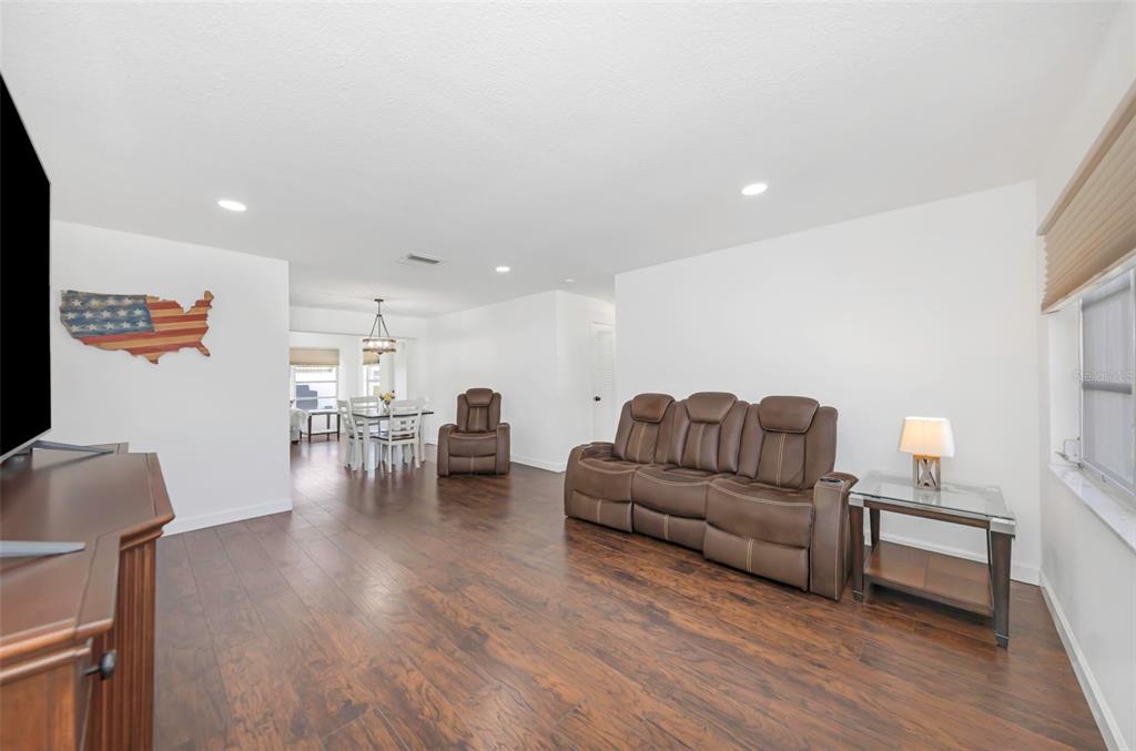 A living room with dark wood flooring, a brown leather sofa, and an adjacent dining area — 4488 100TH AVENUE N, PINELLAS PARK, FL