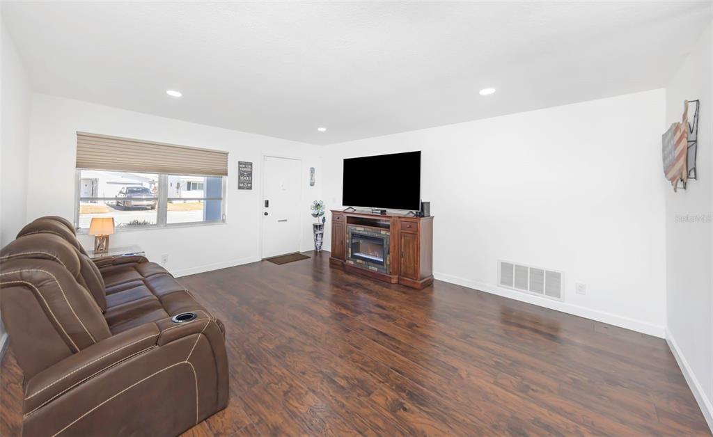 A living room with brown wood flooring, a leather sofa, and a television on a console — 4488 100TH AVENUE N, PINELLAS PARK, FL