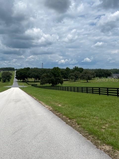 A paved road leads past a black fence bordering a large, grassy pasture with trees — 5610 EAST ORION CT, FLORAL CITY, FL