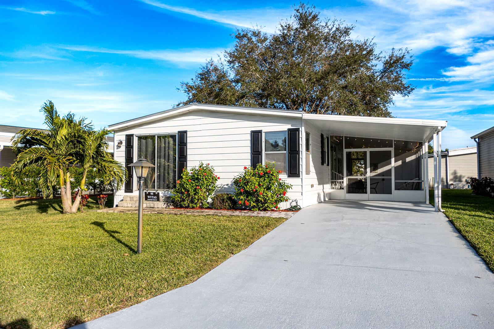 A single-story mobile home with white siding, black shutters, a carport, and a front lawn — 95 N North Warner Drive, Jensen Beach FL 34957, JENSEN BEACH, FL