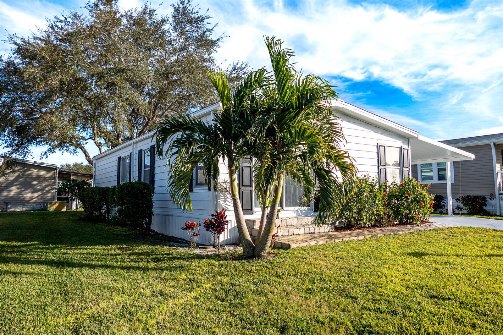 A white mobile home with a palm tree in the front yard under a blue sky — 95 N North Warner Drive, Jensen Beach FL 34957, JENSEN BEACH, FL