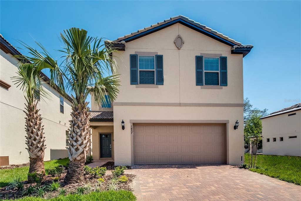 A two-story house with a beige stucco exterior, a two-car garage, and two palm trees — 1857 NICE COURT, KISSIMMEE, FL