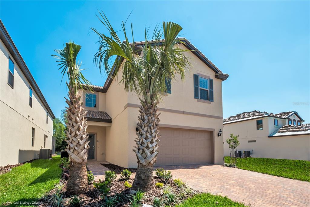A two-story beige house with a two-car garage and two palm trees in front — 1857 NICE COURT, KISSIMMEE, FL