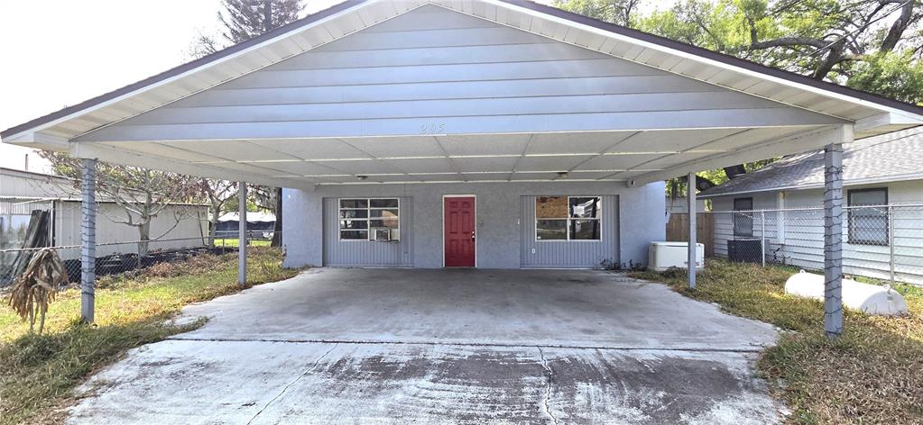 A house exterior features a large concrete carport, a red front door, and gray siding — 205 DIXIE HIGHWAY, AUBURNDALE, FL