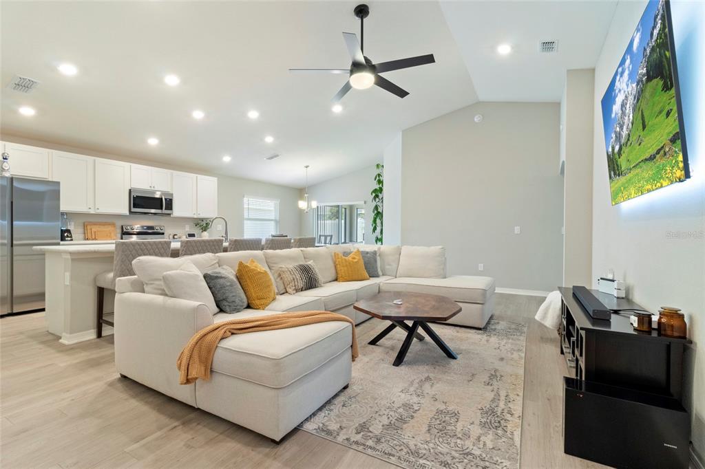 A modern open-concept living room features a large sectional sofa, a wooden coffee table, and a kitchen — 1204 MEZZAVALLE WAY, AUBURNDALE, FL