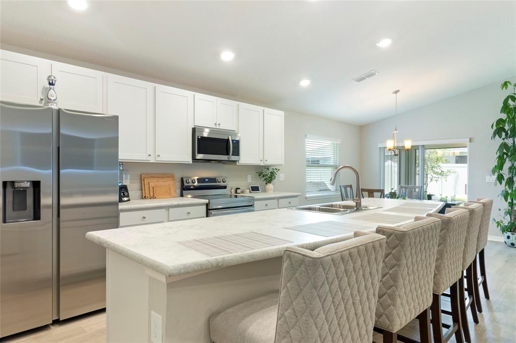 A modern kitchen features white cabinets, stainless steel appliances, and a large island with seating — 1204 MEZZAVALLE WAY, AUBURNDALE, FL