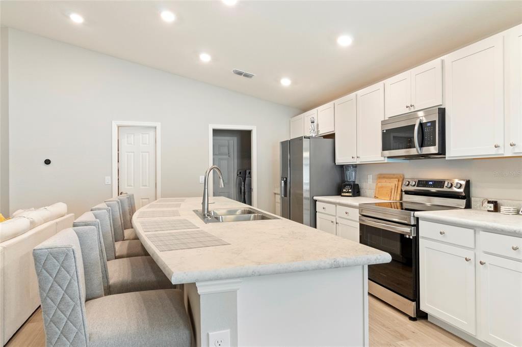 A kitchen features white cabinetry, a curved island with bar seating, and stainless steel appliances — 1204 MEZZAVALLE WAY, AUBURNDALE, FL