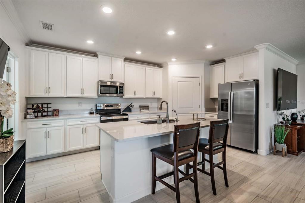 A modern kitchen features white cabinetry, stainless steel appliances, a central island, and tile flooring — 16595 SHELL BAY DRIVE, LAND O LAKES, FL