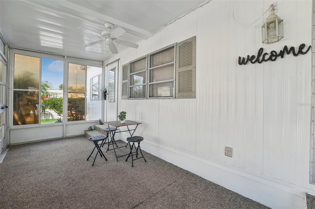 A covered porch features white vertical siding, a ceiling fan, carpeted flooring, and a small table — 1600 N OLD COACHMAN ROAD UNIT 709, CLEARWATER, FL