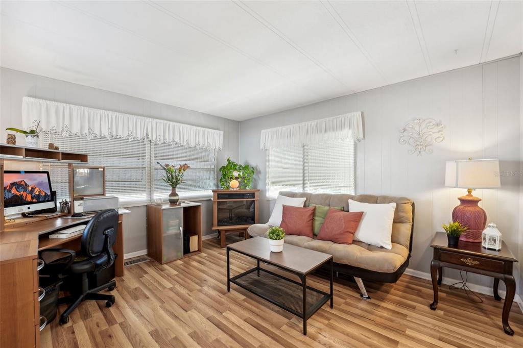 A living room features wood-look flooring, a beige sofa, a desk, and a corner fireplace — 1600 N OLD COACHMAN ROAD UNIT 709, CLEARWATER, FL