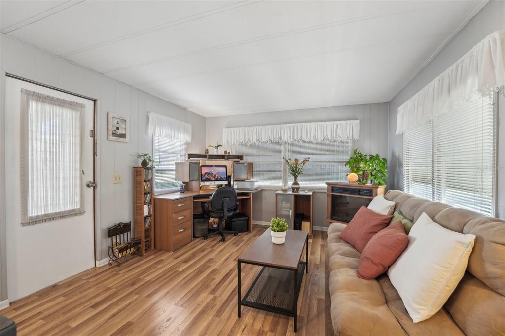 A living room with wood-look flooring, a desk area, a sofa, and large windows — 1600 N OLD COACHMAN ROAD UNIT 709, CLEARWATER, FL