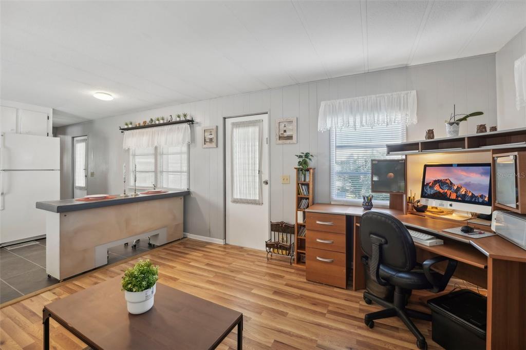 A room with wood-look flooring, a kitchen counter, a desk area, and a white door — 1600 N OLD COACHMAN ROAD UNIT 709, CLEARWATER, FL