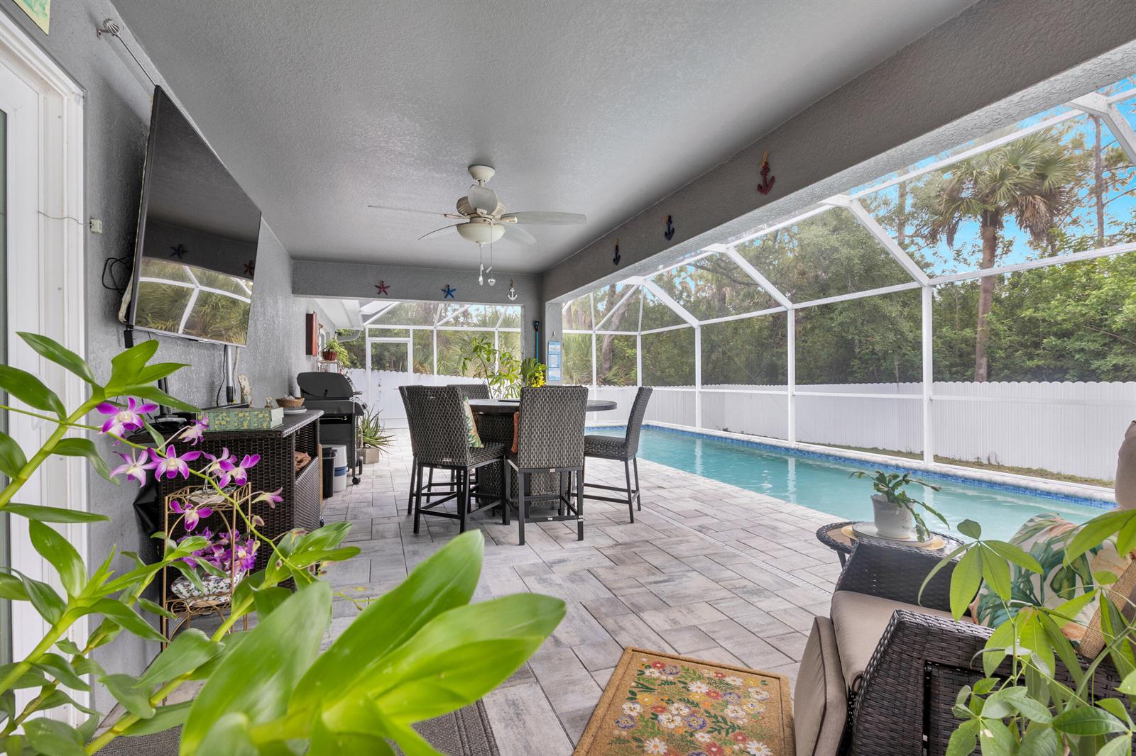 A covered patio features a dining set, a television, and a pool with a screen enclosure — 6034 Twig Court, FL 33935, FL