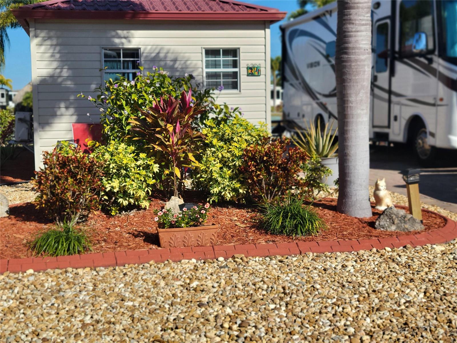 A landscaped garden bed with shrubs and a palm tree sits in front of a house — 551 SW 42nd Cove, Okeechobee FL 34974, OKEECHOBEE, FL