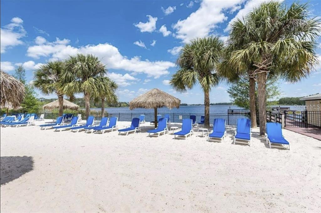 A sandy beach area features rows of blue lounge chairs under palm trees by a lake — 706 GRAN BAHAMA BOULEVARD UNIT 706, DAVENPORT, FL