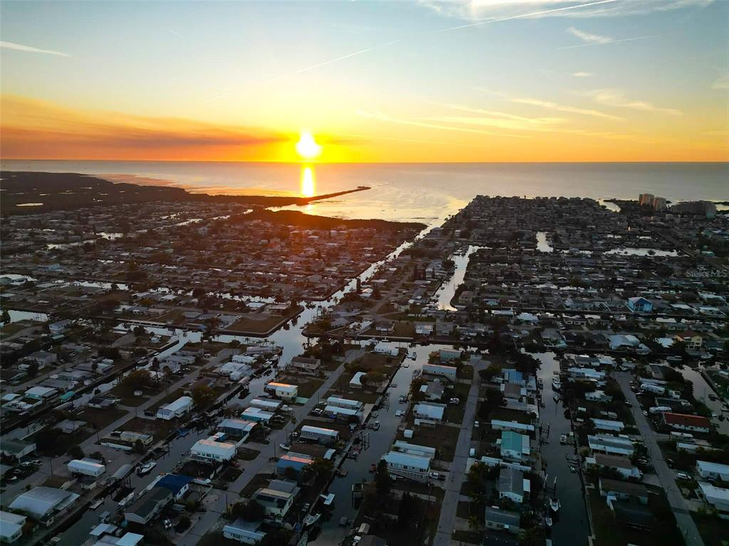 An aerial view shows a coastal neighborhood with residential homes along canals at sunset — 6814 GULL LANE, HUDSON, FL
