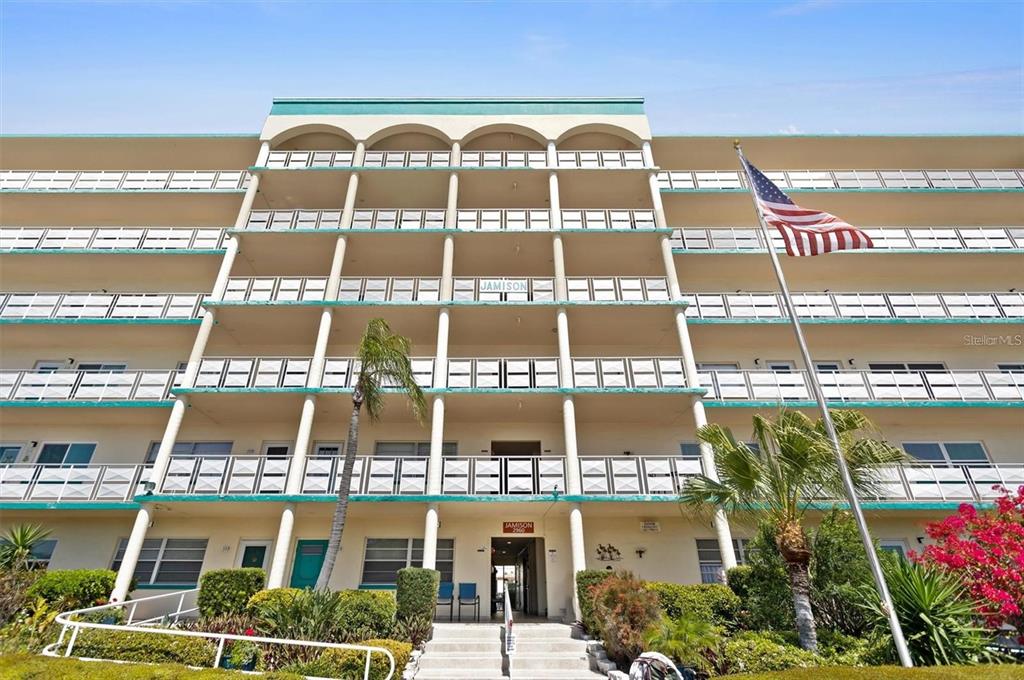 A multi-story apartment building exterior features white balconies, a central entrance, and an American flag — 2960 59TH STREET S UNIT 105, GULFPORT, FL