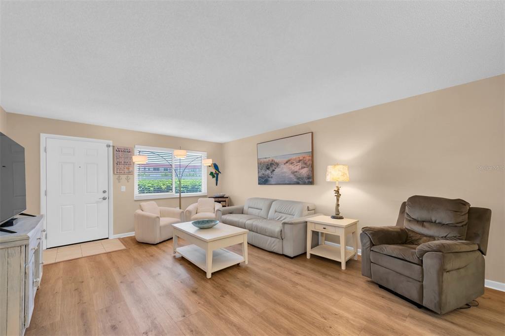 A living room features light wood-look flooring, beige walls, a sofa, and a recliner — 2960 59TH STREET S UNIT 105, GULFPORT, FL