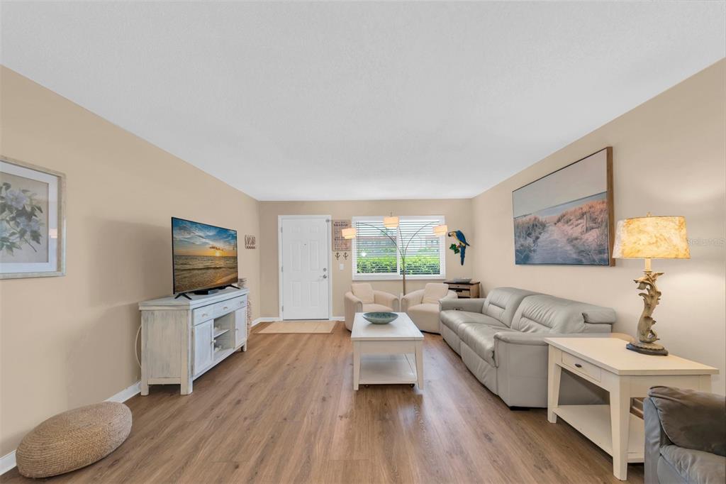 A living room features light wood-look flooring, a white sofa, and a television on a console — 2960 59TH STREET S UNIT 105, GULFPORT, FL