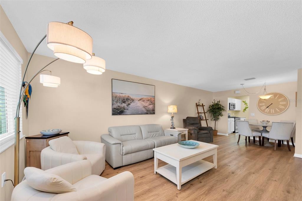 A living room with light wood floors, a white sofa, two armchairs, and a dining area — 2960 59TH STREET S UNIT 105, GULFPORT, FL